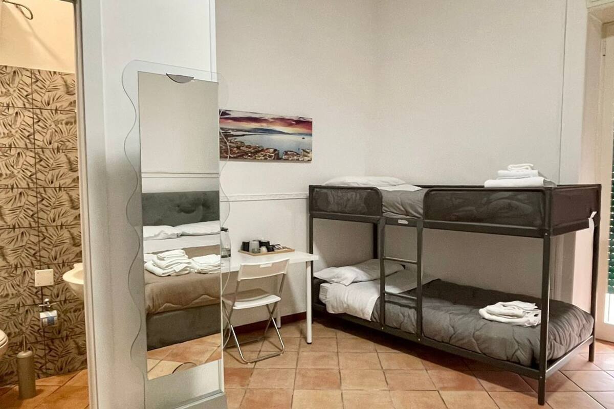A compact room with bunk beds, a desk, and a chair. There is a small table with a bottle and a cup, and a painting on the wall.