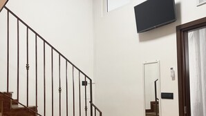 A staircase with wooden steps and metal railings, a mounted air conditioner, a flat-screen TV, and a mirror on the wall. - House Caracciolo (Naples)