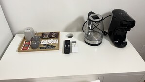 A white desk with a coffee maker, a remote control, a glass carafe, and a tray with coffee pods and a mug. - House Caracciolo (Naples)