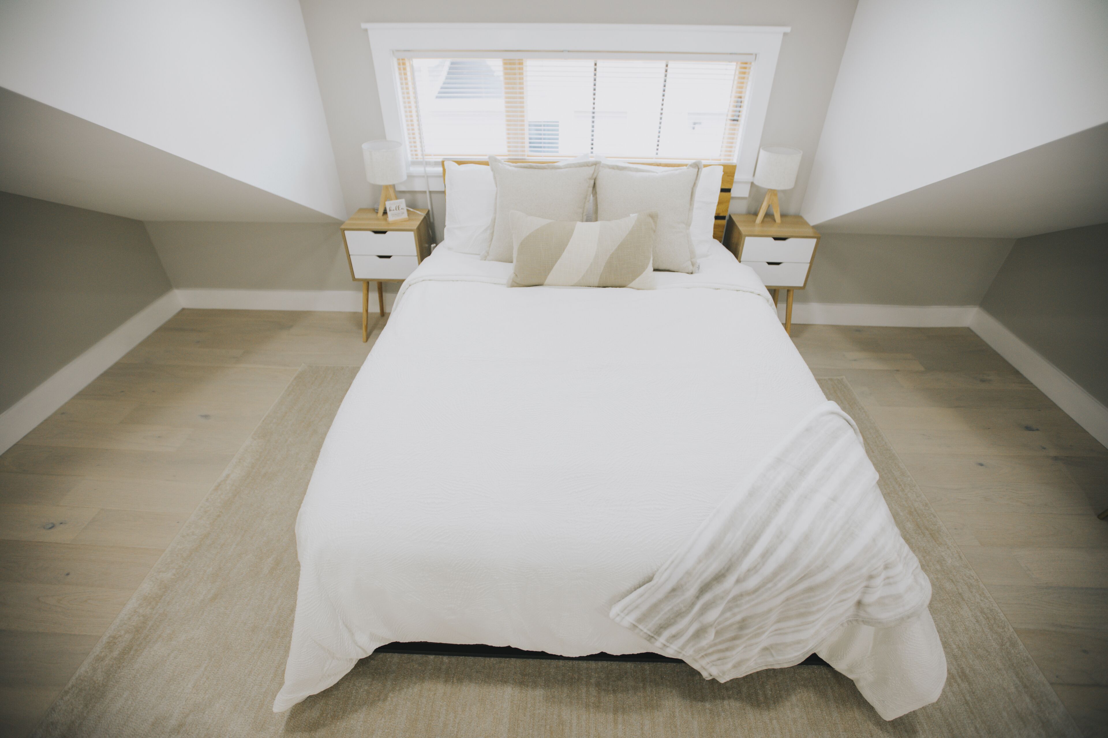 A bedroom with a large bed, two bedside tables, and a window with blinds.