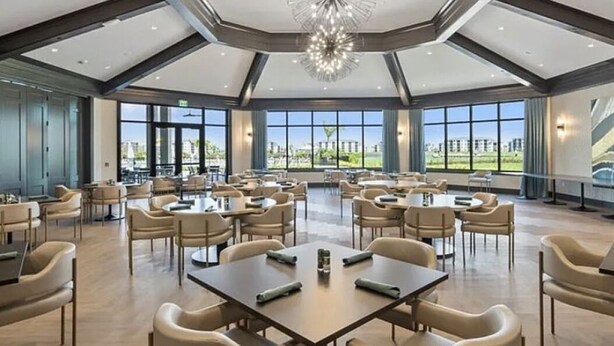 Un'ampia sala da pranzo con diversi tavoli e sedie, grandi finestre che offrono vista sull'esterno e un moderno lampadario.