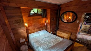 A wooden cabin bedroom with a bed, bedside lamps, a mirror, and a fan. - A romantic night in a Hole in the Ground (Tauwhare)