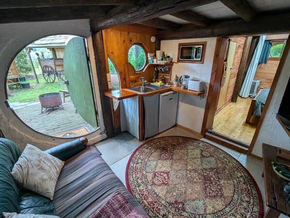 A cozy, rustic kitchen with a wooden interior, a sink, and a microwave. A large round window offers a view of the outdoors.