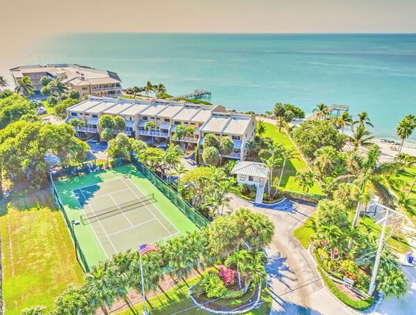 An aerial view of a resort with multiple buildings, a tennis court, and a beach. - Stunning 180° Open Water Views (Key Colony Beach)