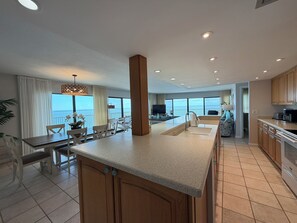 A modern kitchen with a central island, dining area with chairs, and a view of the sea. - Stunning 180° Open Water Views (Key Colony Beach)