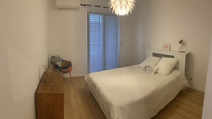 A bedroom with a bed, a desk, a chair, and a window with blinds.