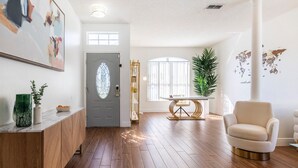 Un salon spacieux doté d’un parquet, d’un fauteuil blanc, d’une table à manger avec un pied doré et d’un grand tableau abstrait accroché au mur.