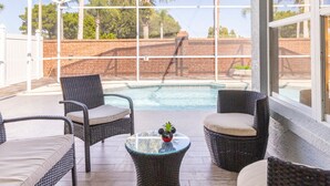 Un espace extérieur abrité, aménagé avec des meubles en osier, une table en verre et une piscine.