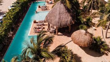 An aerial view of a resort with a rectangular swimming pool, lounge chairs, and thatched-roof structures.