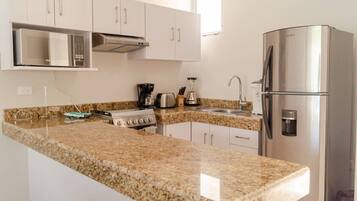 A modern kitchen with white cabinets, a granite countertop, a built-in microwave, a stove, a refrigerator, and a coffee maker.