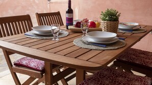 Una mesa de comedor de madera con platos, copas y una botella de vino tinto.