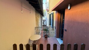 Un estrecho callejón con cerca de madera, una mesa y silla blancos, y una planta en maceta.