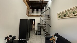 Amplia zona de estar con un sofá negro, un mueble negro, una escalera con barandilla de madera y un candelabro.