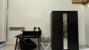 Una habitación con un escritorio negro, una silla negra, una silla plegable blanca y un armario negro con espejo.