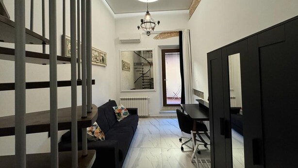 Una sala de estar moderna con un sofá oscuro, una mesa de comedor y una escalera que sube a otro nivel.
