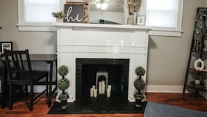 A white fireplace with a mantel shelf, flanked by two small potted plants. - Short Drive to Friends Uni - Quaint Cottage W/ W&D (Wichita)