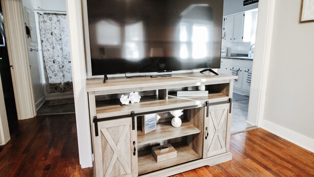 A wooden entertainment center with a flat-screen TV, built-in shelves, and a lower cabinet with drawers. - Short Drive to Friends Uni - Quaint Cottage W/ W&D (Wichita)