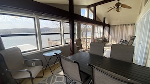 Ein sonnendurchfluteter Raum mit Seeblick, ausgestattet mit Tisch, Stühlen, Deckenventilator und großen Fenstern.
