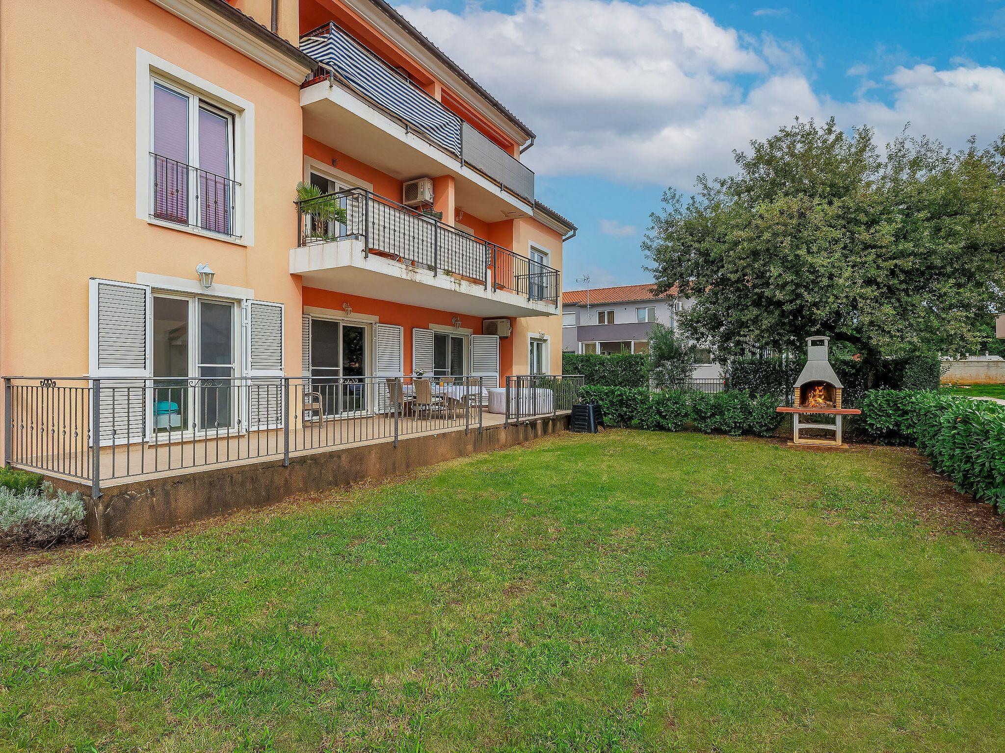 A two-story residential building with balconies, a small outdoor seating area, and a wood-burning stove.