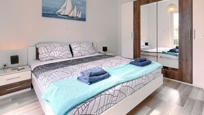 A modern bedroom with a bed, bedside tables, a large mirror, and a painting of sailboats.