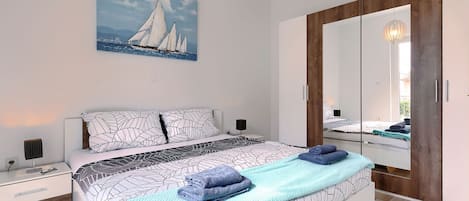 A modern bedroom with a bed, bedside tables, a large mirror, and a painting of sailboats.