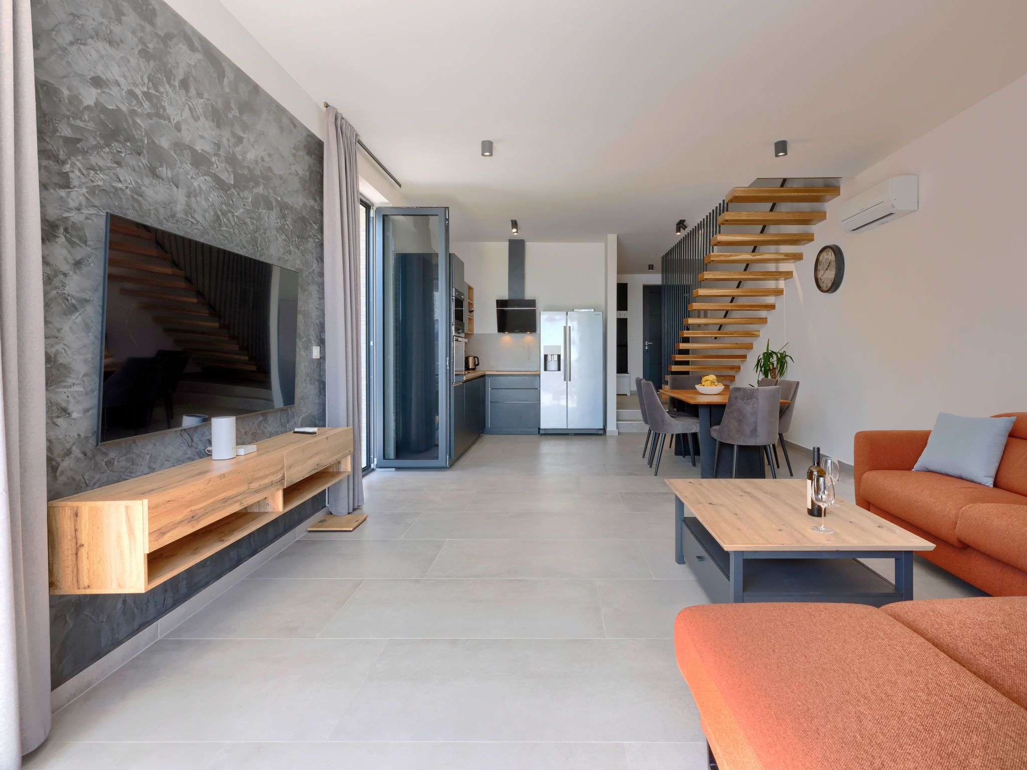Ein modernes Wohnzimmer mit großem Fernseher, einem Holztisch und einem orangefarbenen Sofa.