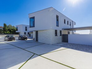 A modern two-story house with a garage, parked cars, and a clear blue sky.