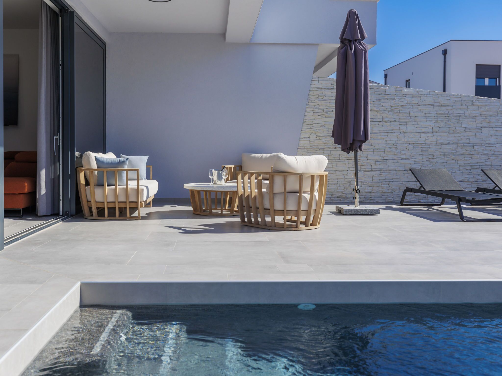 An outdoor pool area with lounge chairs, a table, and an umbrella.