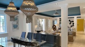 Uma área de refeições moderna com mesa de vidro, cadeiras azuis e luminárias pendentes decorativas.
