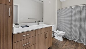 A modern bathroom with wooden cabinets, a white sink, a large mirror, and a shower curtain with a geometric pattern. - The Platinum Suite Penthouse The Gulch  (Nashville)