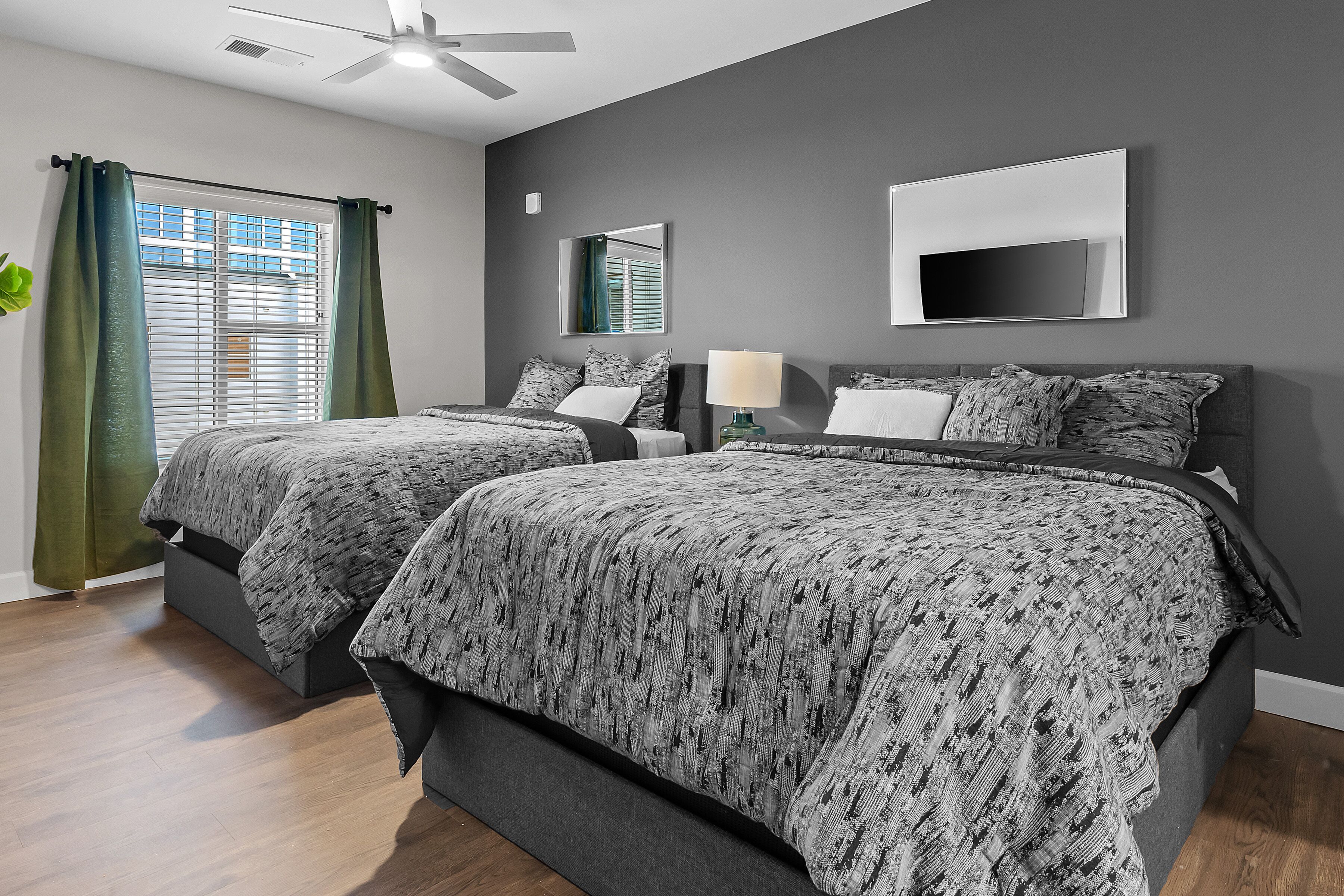 A modern bedroom with two beds, a ceiling fan, a TV, and a window with curtains.