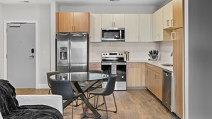A modern kitchen with stainless steel appliances, wooden cabinets, and a dining area with a glass table and chairs. - The Platinum Suite Penthouse The Gulch  (Nashville)