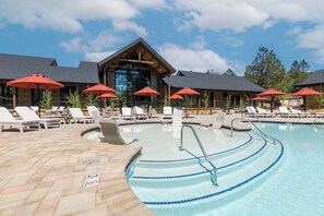 A pool area with lounge chairs and umbrellas, a wooden building with large windows, and a clear sky.