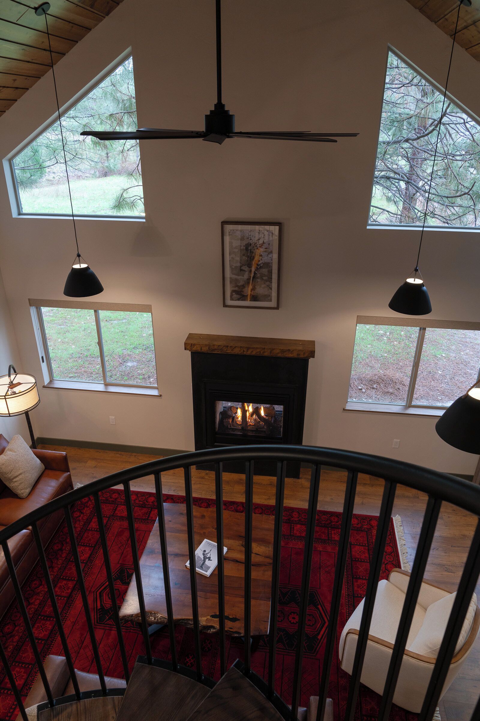 A spacious living room with a fireplace, large windows, and a staircase leading to an upper level.