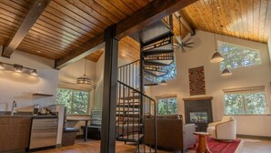 A spacious living area with a wooden ceiling, a fireplace, and a staircase.