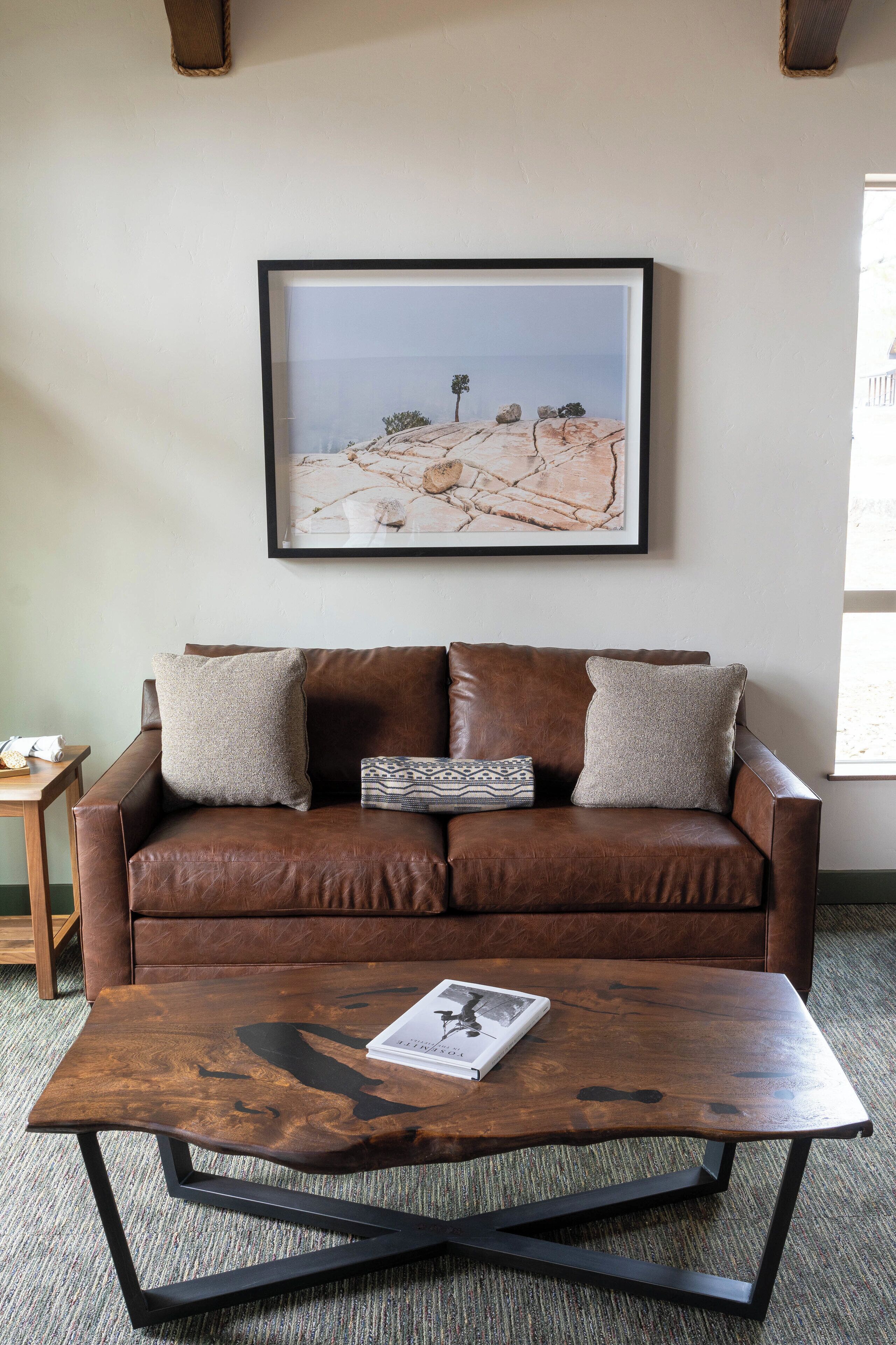 A brown leather sofa with two pillows and a framed artwork above it.