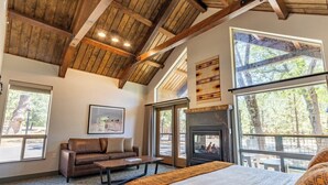 A spacious room with a large bed, a fireplace, a leather sofa, and large windows offering a view of the outdoors.