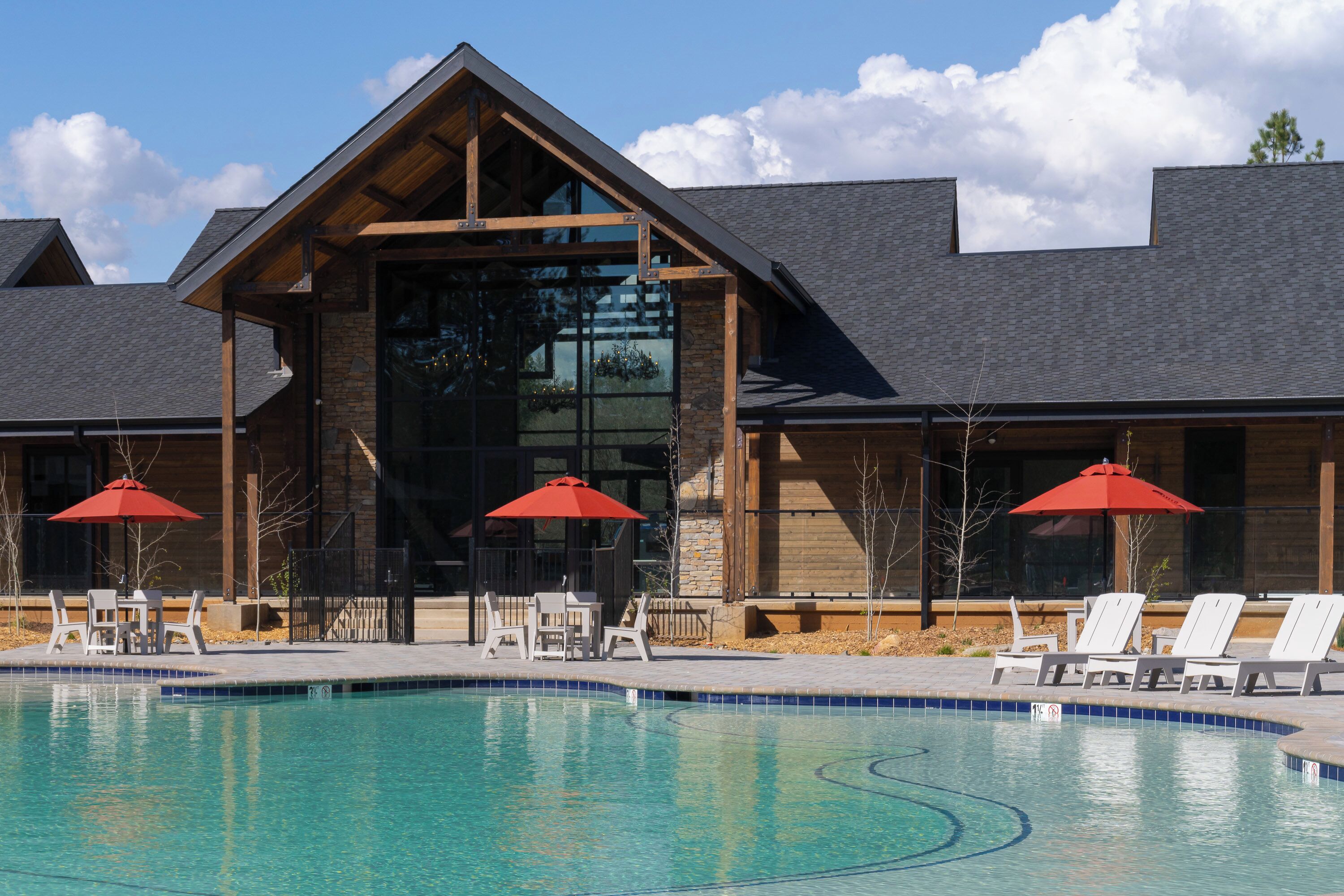 A modern building with a swimming pool, outdoor seating, and large windows.