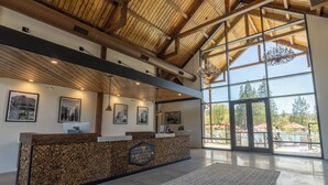 A reception area with a wooden reception desk, framed artwork on the walls, and large windows offering a view of outdoor seating and a pool.