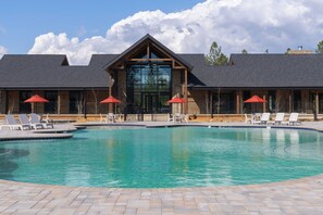 A pool area with lounge chairs and umbrellas, a building with a large glass entrance, and a clear sky.