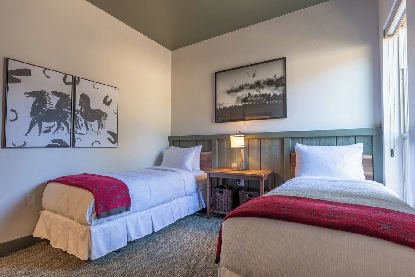 A hotel room with two beds, a nightstand, a lamp, and artwork on the walls.