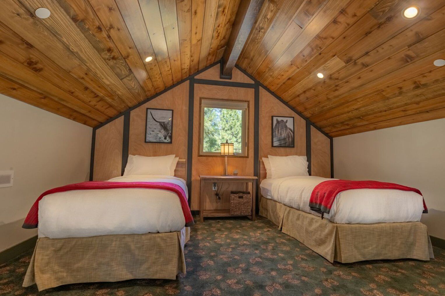 Una habitación con dos camas, vigas de madera en el techo, una ventana y una mesita con una lámpara.