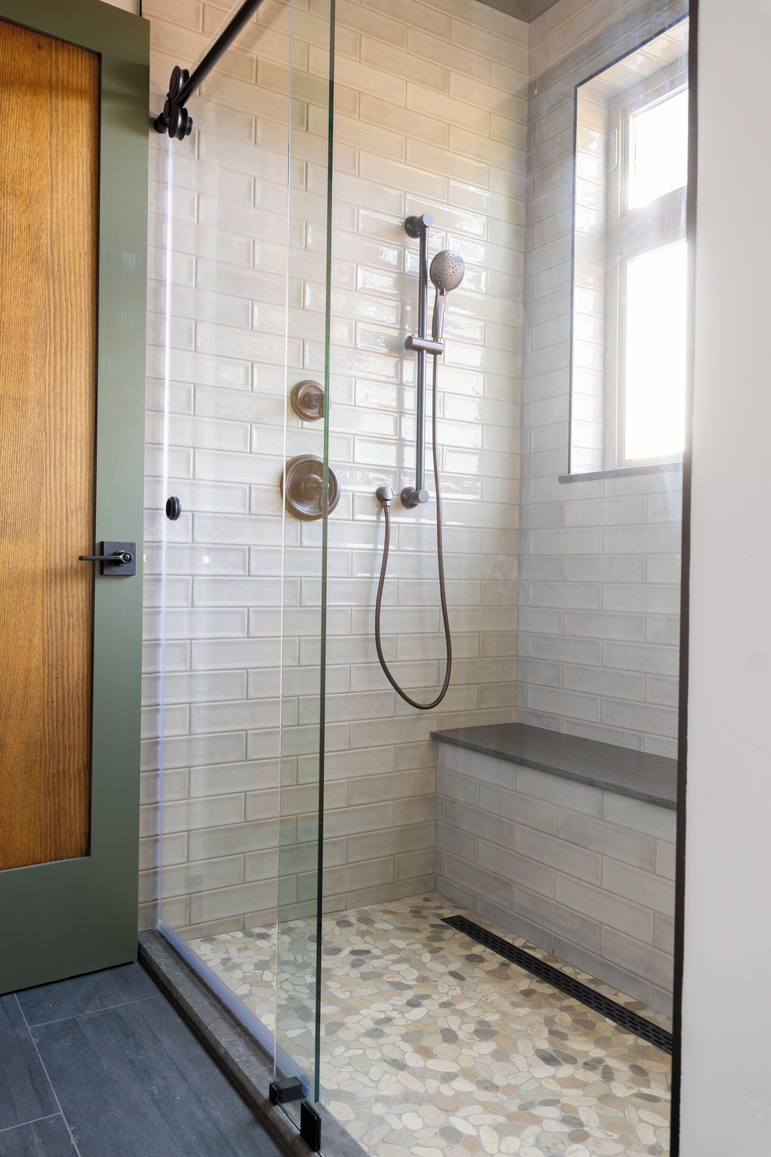 A glass-enclosed shower with white tiled walls and a pebble-patterned floor.