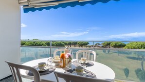 A balcony table with chairs, a glass table, and a view of the sea and greenery. - Le Mireille by Interhome (Le Grau du Roi)