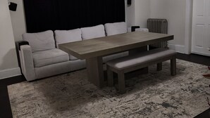A room with a large flat-screen TV, a dining table with benches, a sofa, and a radiator. - Spacious and luxurious 3-bedroom home w/jetted bathtub (Worcester)