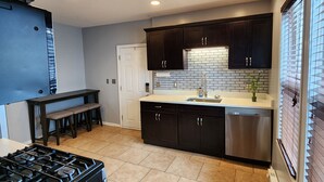 A modern kitchen with dark cabinetry, a stainless steel dishwasher, and a tiled floor. - Spacious and luxurious 3-bedroom home w/jetted bathtub (Worcester)