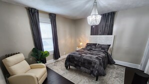 A bedroom with a bed, a chair, a nightstand, a lamp, and a plant. - Spacious and luxurious 3-bedroom home w/jetted bathtub (Worcester)