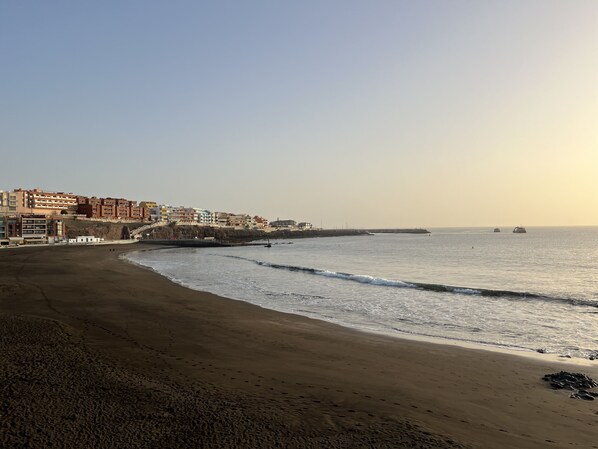 A beach with a promenade, buildings, and a pier extending into the sea.