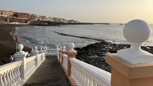 A seaside promenade with a stone pathway leading to the beach, white balustrades, and a view of the ocean.