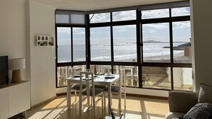 A dining area with a large bay window overlooking a beach.